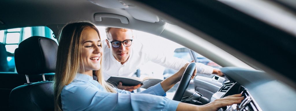 Woman sitting in a car while a salesman assists her.